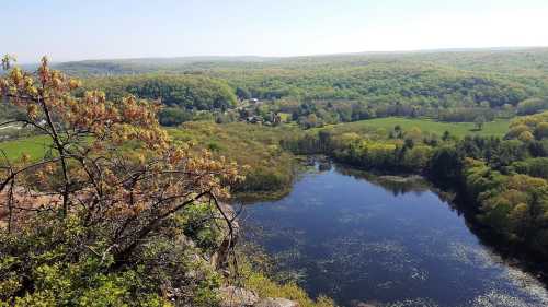 A scenic view from a rocky overlook, showcasing lush green hills and a calm lake surrounded by trees.