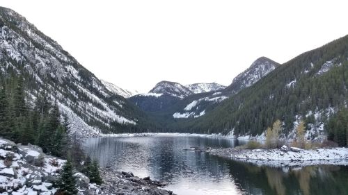 A serene mountain lake surrounded by snow-capped peaks and evergreen trees, reflecting the calm sky.