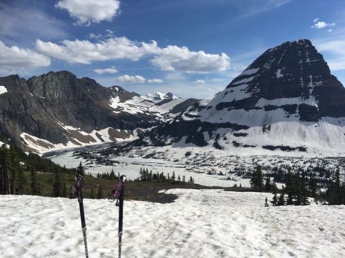 Snow-covered mountains and a valley under a blue sky, with ski poles in the foreground.