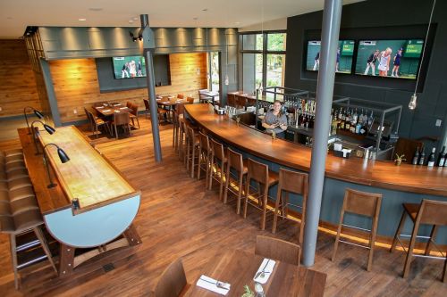 A modern restaurant interior featuring a bar, wooden decor, and multiple screens showing sports.