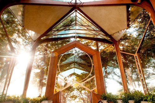 A modern glass structure surrounded by trees, reflecting sunlight and nature, creating a serene atmosphere.