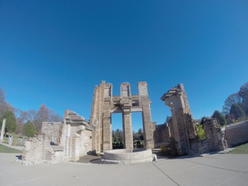 Ruins of a stone structure under a clear blue sky, surrounded by greenery and pathways.