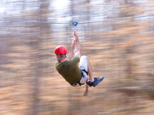 A person in a red helmet zip-lining through a forest, with blurred trees in the background.