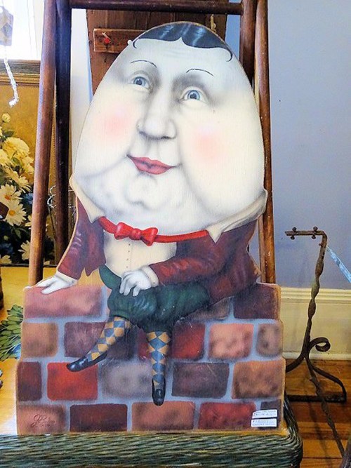 A whimsical, oversized figure of Humpty Dumpty sitting on a brick wall, wearing a bow tie and colorful stockings.