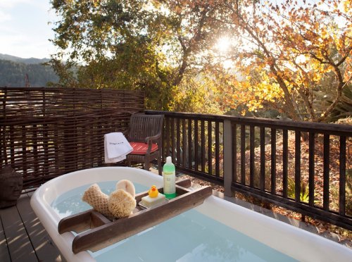 A serene outdoor bathtub on a deck, surrounded by trees and autumn leaves, with a view of the sunset.