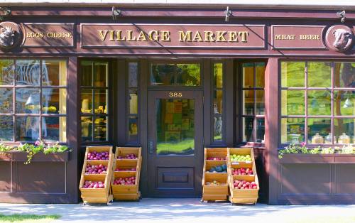 A charming village market with wooden crates of colorful apples outside and a welcoming entrance.