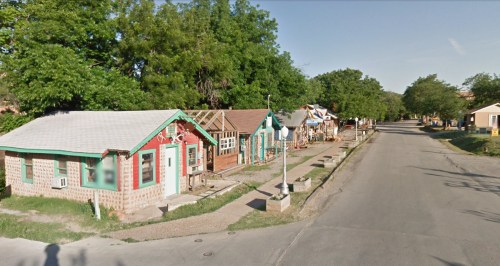 A quiet street lined with colorful, small houses and trees on a sunny day.
