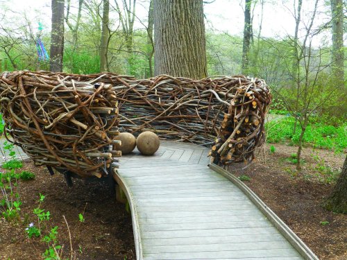 A large, nest-like structure made of branches sits beside a wooden walkway in a forested area.