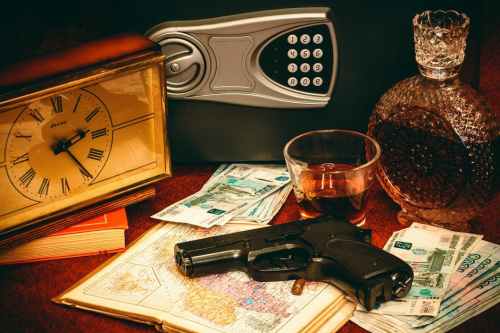 A handgun rests on a map, surrounded by cash, a clock, a whiskey glass, and a safe.