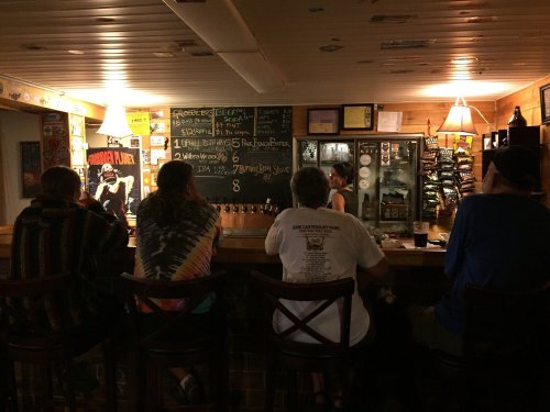 A cozy bar scene with patrons sitting at the counter, a chalkboard menu, and a bartender serving drinks.