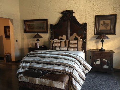 Cozy bedroom featuring a wooden bed, patterned bedding, and rustic decor with lamps and artwork on the walls.