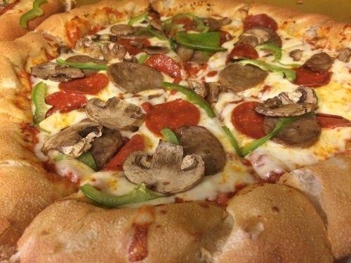 A close-up of a pizza topped with pepperoni, sausage, green peppers, and mushrooms, featuring a stuffed crust.