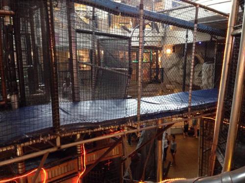 A view of a multi-level indoor play structure with netting and a blue walkway, bustling with activity below.