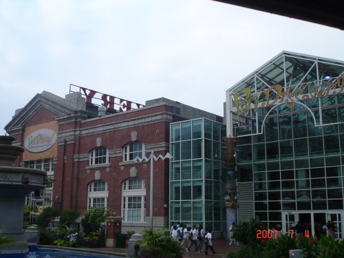 A view of a large building with a glass facade and a brick structure, featuring colorful signage.