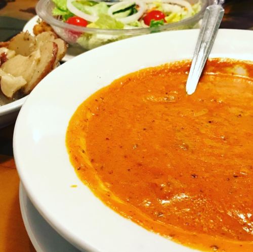 A bowl of creamy orange soup with a spoon, accompanied by a fresh salad and a side of potatoes.