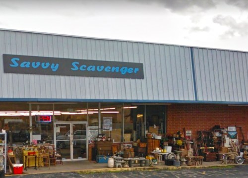 Exterior of "Savvy Scavenger" store, showcasing various antiques and items for sale outside under a cloudy sky.