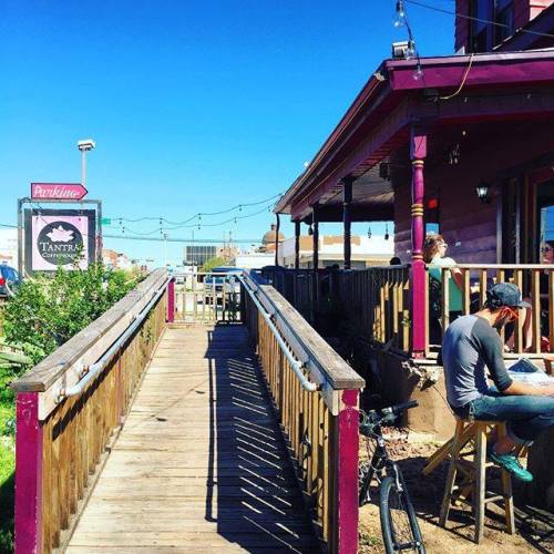A wooden walkway leads to a colorful building with outdoor seating, surrounded by clear blue skies.