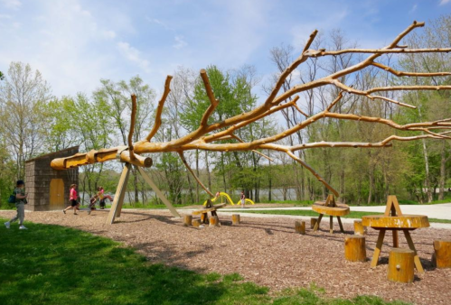 A unique playground with wooden structures, swings, and children playing in a green park setting.