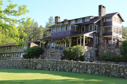 A large, rustic house with stone accents, surrounded by green grass and trees, set against a clear blue sky.