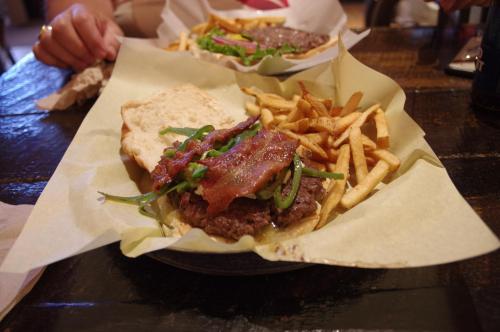 A close-up of a burger with bacon, green peppers, and fries on a plate, set on a wooden table.
