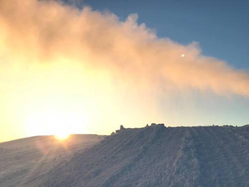 A snowy landscape at sunrise, with soft clouds illuminated by the golden light of the sun.