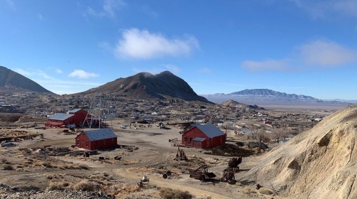 A panoramic view of a historic mining town with red buildings, mountains, and a clear blue sky in the background.