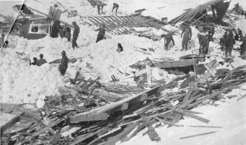 Rescue workers search through snow and debris after a building collapse, with several people visible in the scene.