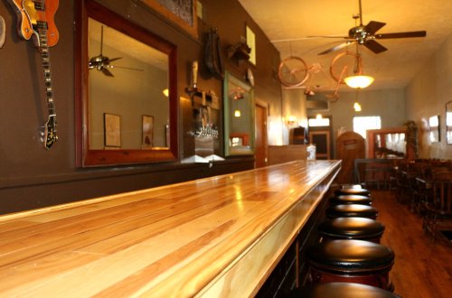 A wooden bar with black stools, mirrors, and guitars on the wall in a cozy, rustic interior.
