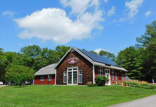 A red and brown building with solar panels on the roof, surrounded by green grass and trees under a blue sky.