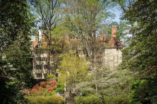 A historic building surrounded by lush greenery and blooming flowers on a sunny day.