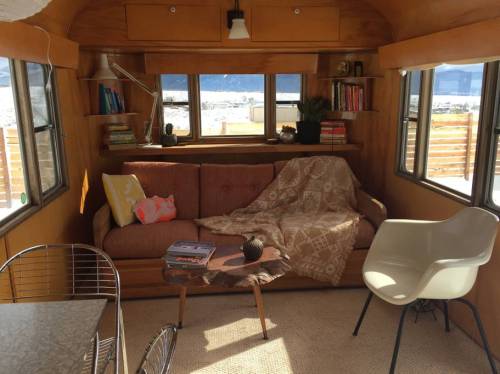 Cozy interior of a vintage trailer with a sofa, coffee table, and large windows showcasing a scenic view.