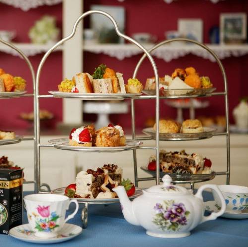 A tiered stand filled with assorted pastries and sandwiches, accompanied by a teapot and teacups on a blue tablecloth.