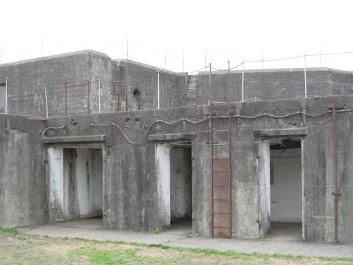 A weathered concrete structure with multiple doorways and a ladder, set against a cloudy sky.