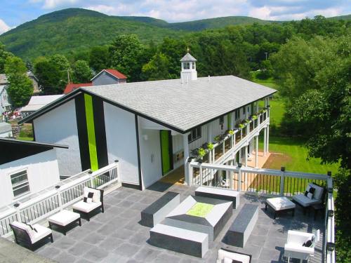 A modern building with a green and white exterior, surrounded by trees and mountains, featuring a rooftop patio with seating.