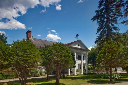 A charming white house with a porch, surrounded by green trees and a blue sky with fluffy clouds.