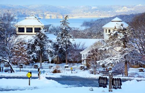 A snowy landscape featuring a charming building with a lake in the background and trees dusted with snow.
