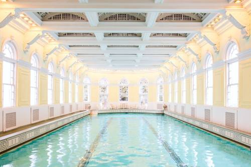 Bright indoor swimming pool with large windows and elegant architectural details, featuring light yellow walls and water.