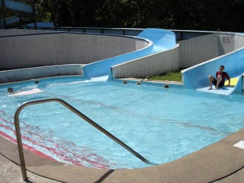A water park scene featuring a blue slide and a pool, with two people enjoying the water.