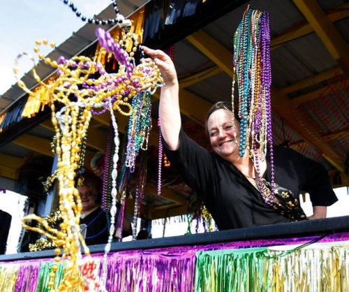 A woman on a festive float joyfully throws colorful beads during a parade celebration.