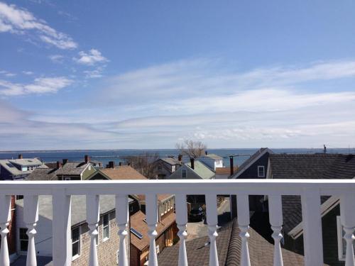 A view from a balcony overlooking rooftops and a calm ocean under a clear blue sky with scattered clouds.