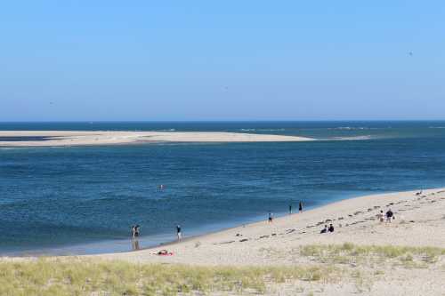 A serene beach scene with people walking along the shore, gentle waves, and a clear blue sky.