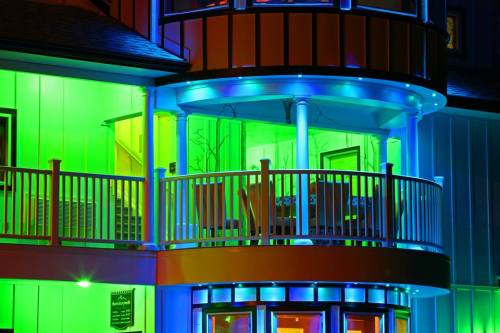 A brightly lit building with colorful green and blue lights illuminating the balcony and exterior.