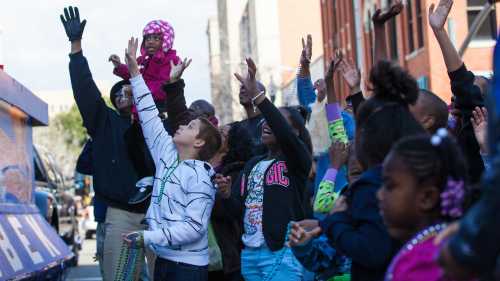 A crowd of diverse children and adults joyfully reaching up, celebrating during a festive event.