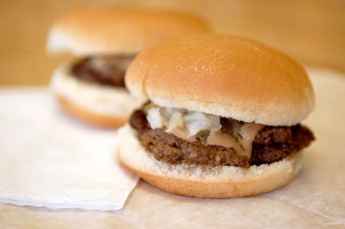 Two small hamburger sandwiches with a beef patty, onions, and sauce on soft buns, placed on a napkin.