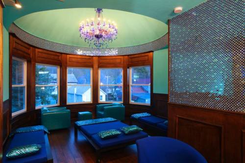A cozy room with teal walls, a chandelier, and lounge seating, featuring large windows with a view of the outdoors.