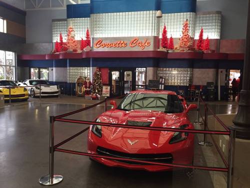 A red Corvette in front of the Corvette Cafe, decorated for Christmas with festive trees and lights.
