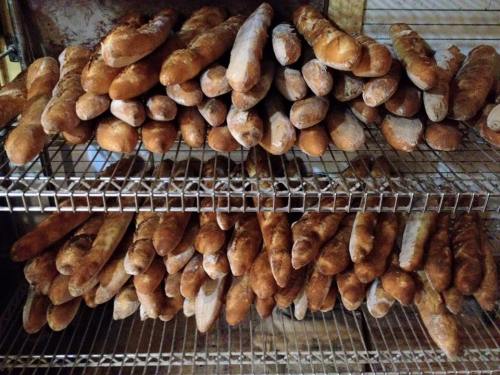 A display of freshly baked baguettes stacked on wire racks in a bakery.