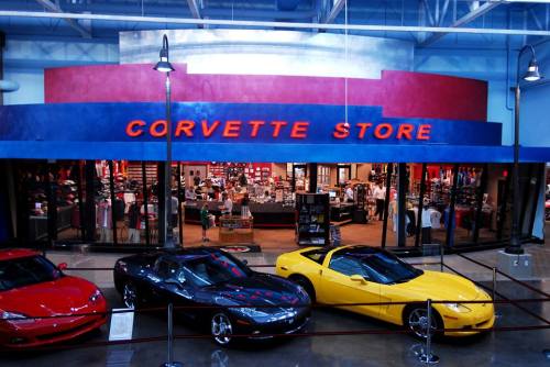 Exterior view of the Corvette Store featuring three colorful Corvettes: red, yellow, and black, with merchandise visible inside.