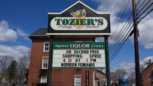 Sign for Tozier's Family Market featuring a liquor store announcement for a free shopping spree on April 21 at 1 PM.