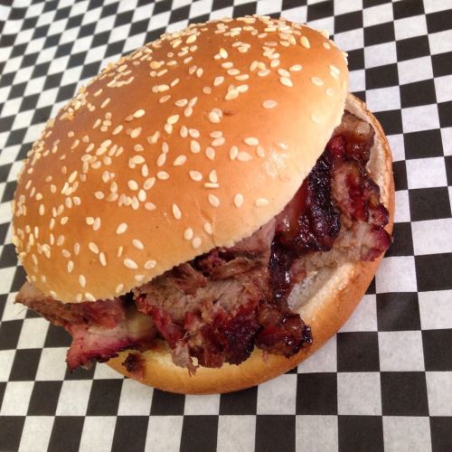A sesame seed bun filled with smoky, sliced barbecue meat, resting on a black and white checkered surface.